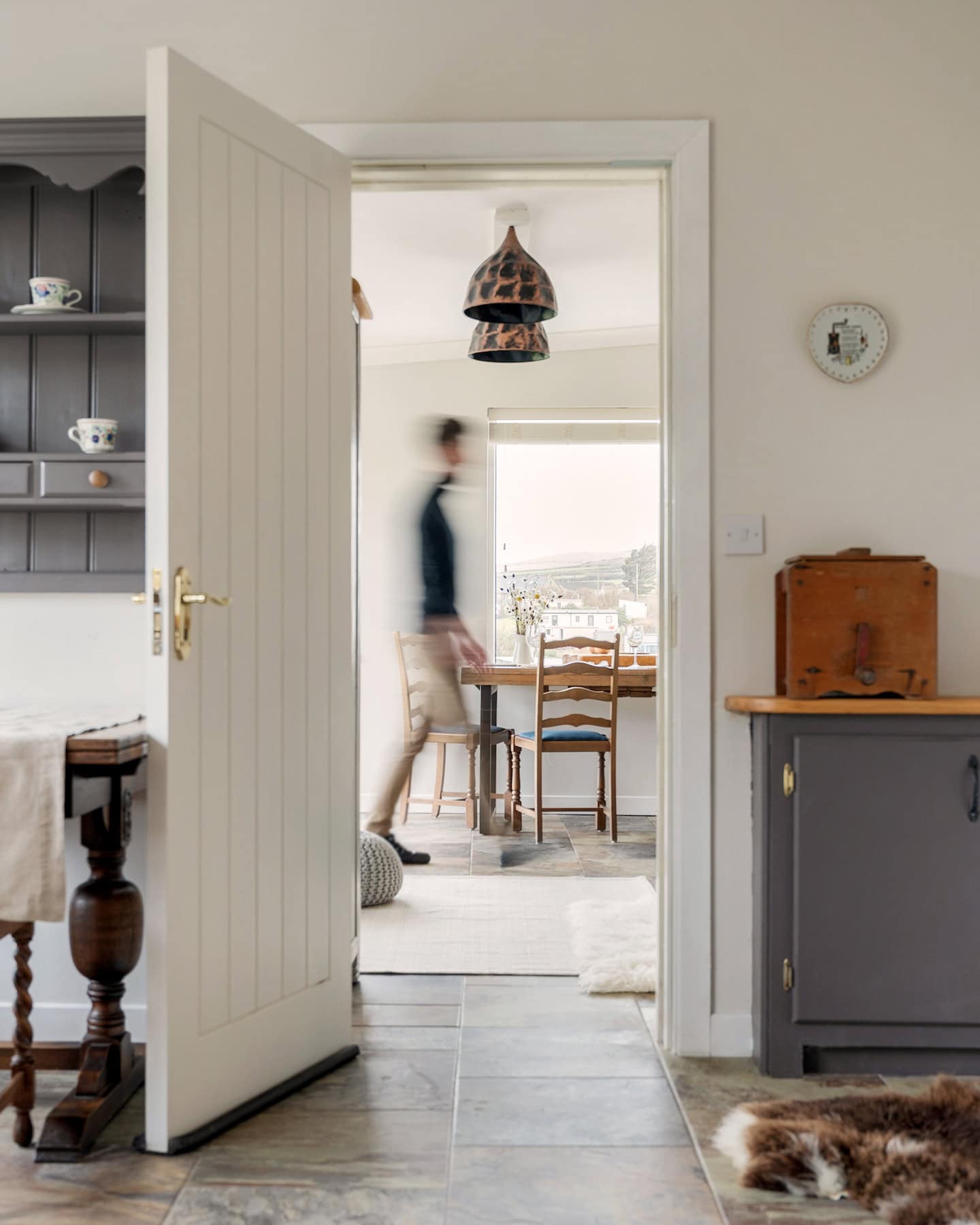 View from Pipers Cottage into the neighbouring Ocean Blue property, with a guest walking through the open doorway and countryside scenery visible beyond the dining area.