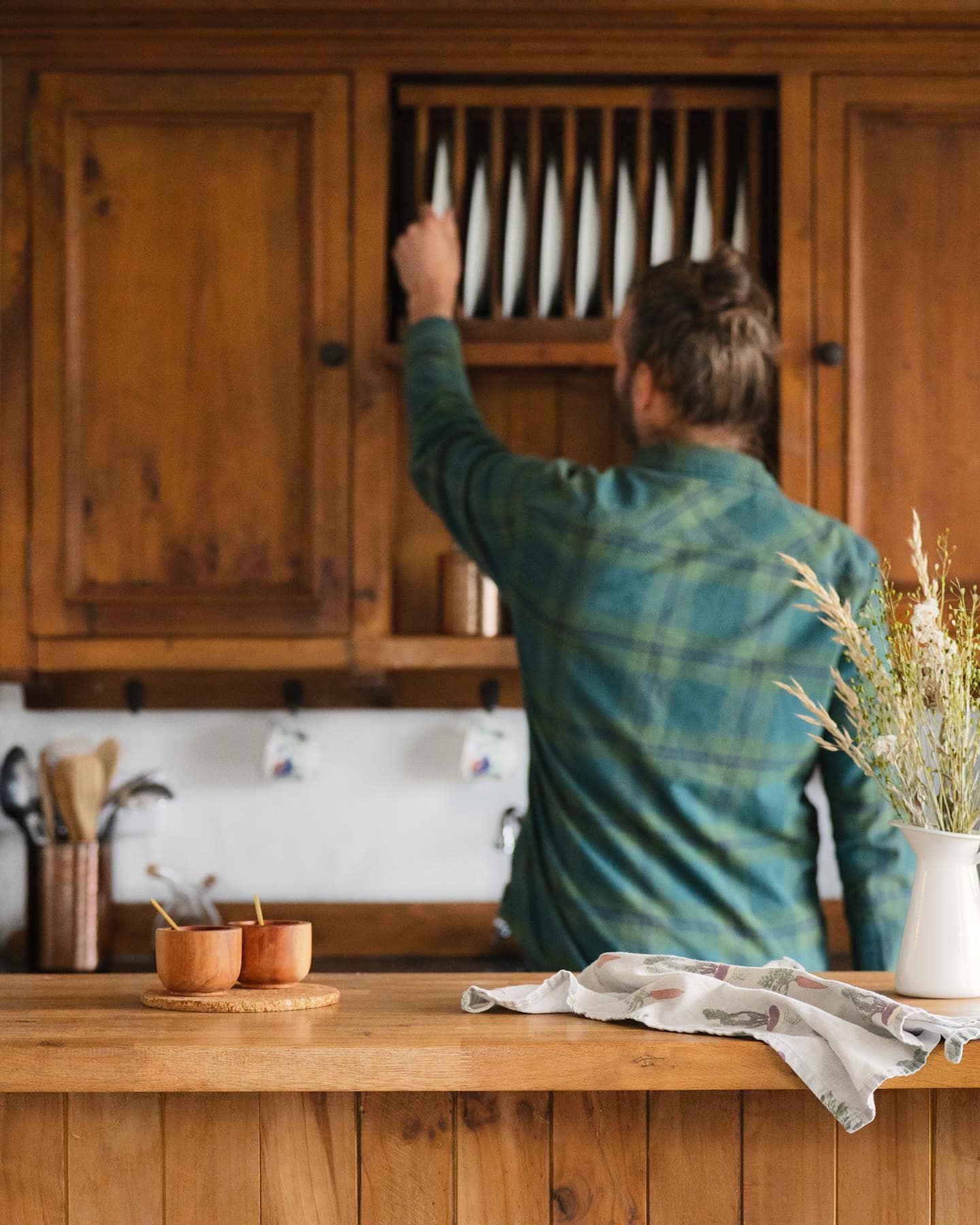 Guest reaching for a plate in the rustic wooden kitchen of Pipers Cottage, a cozy holiday rental with countryside charm.