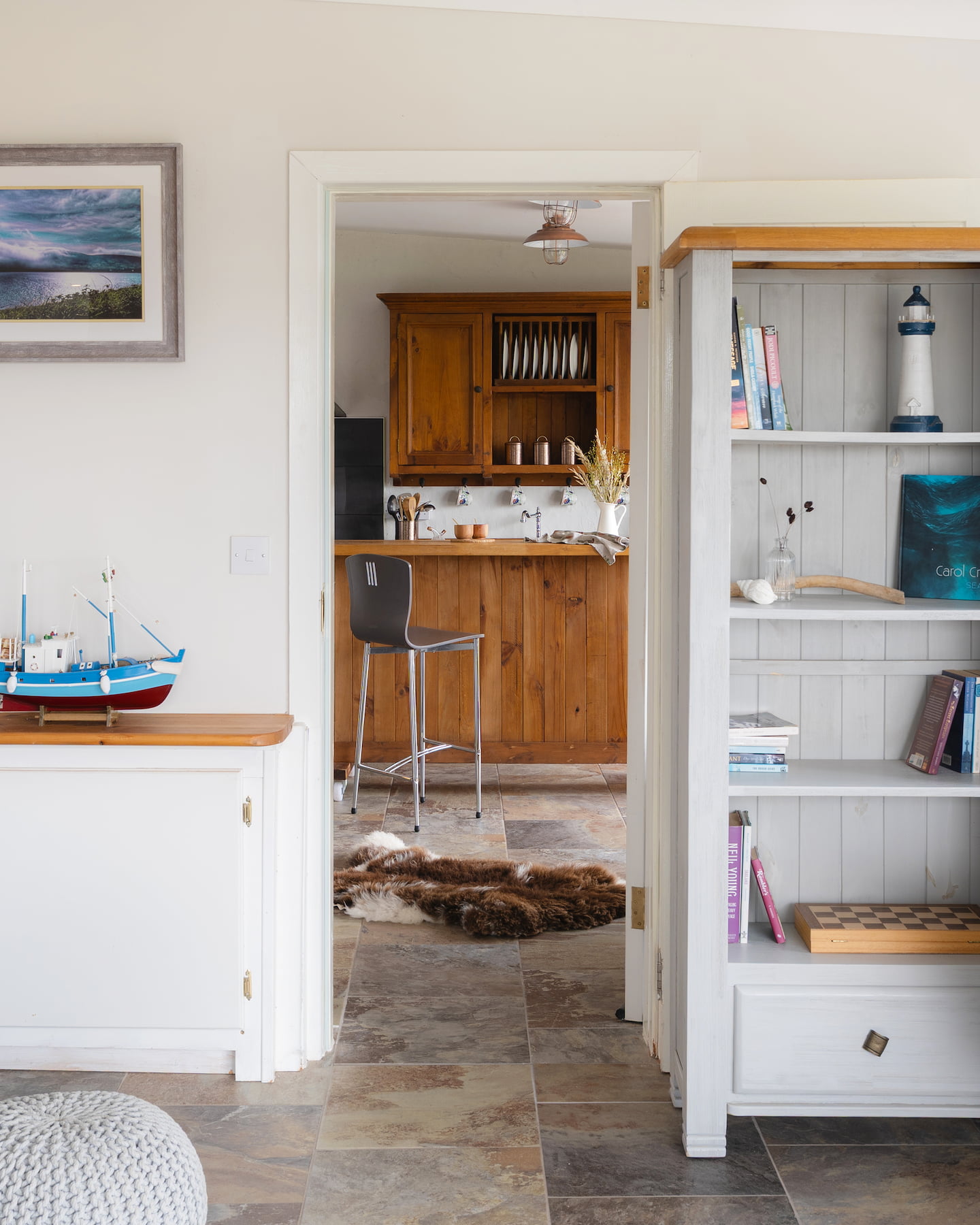 View from Ocean Blue’s living room into adjoining Pipers Cottage via connecting door, ideal for group bookings at Sanctuary Cottages in Dingle. Features coastal décor, tiled flooring, and open-plan kitchen cabinetry.