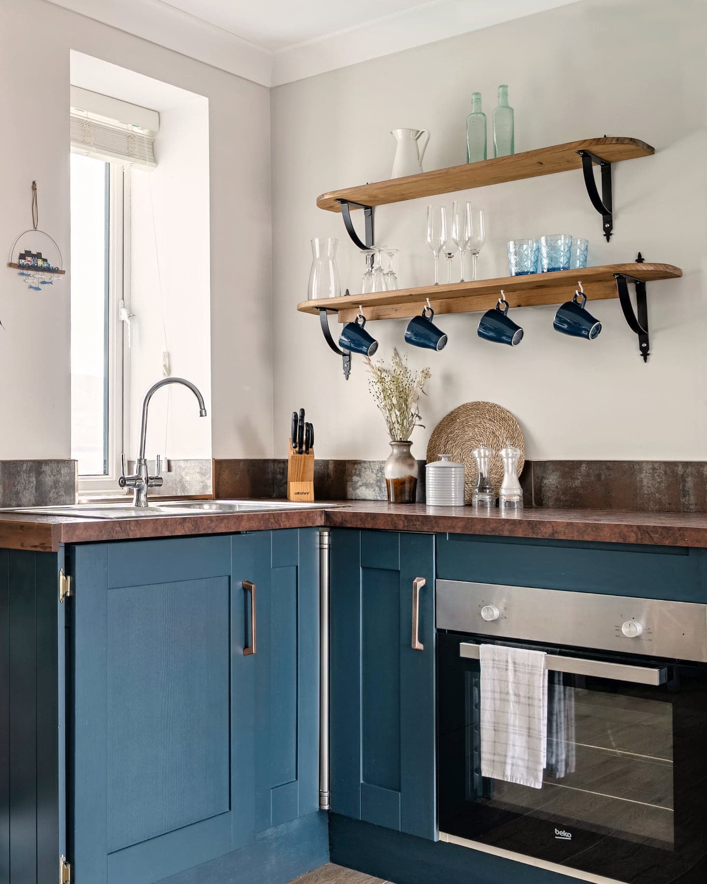 Stylish, fully equipped kitchen at Ocean Blue, Sanctuary Cottages in Dingle, featuring deep blue shaker cabinets, open wooden shelving with glassware, and a modern electric oven.