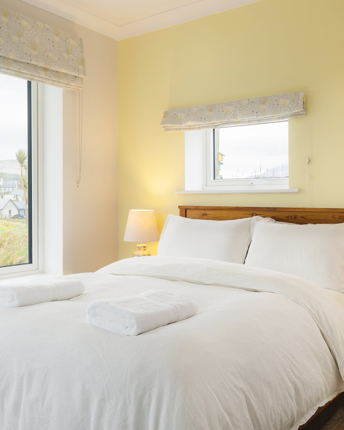 Bright and inviting master bedroom at Ocean Blue, Sanctuary Cottages in Dingle, featuring a crisp white duvet, soft lighting, and dual-aspect windows with views across the bay.