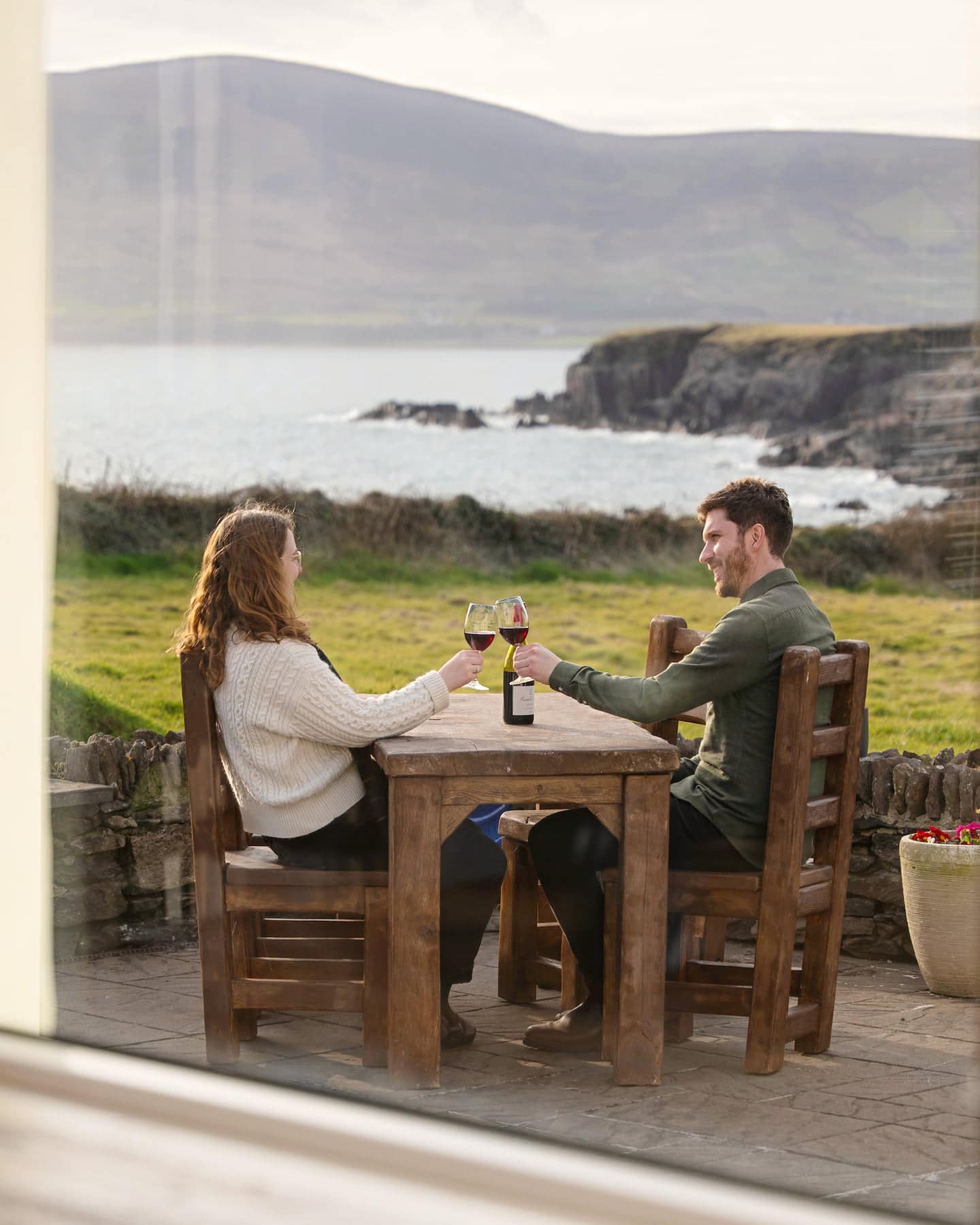 Couple enjoying wine on the private patio at Ocean Blue, Sanctuary Cottages in Dingle, with panoramic views across Ventry Bay and the dramatic cliffs of the Dingle Peninsula.